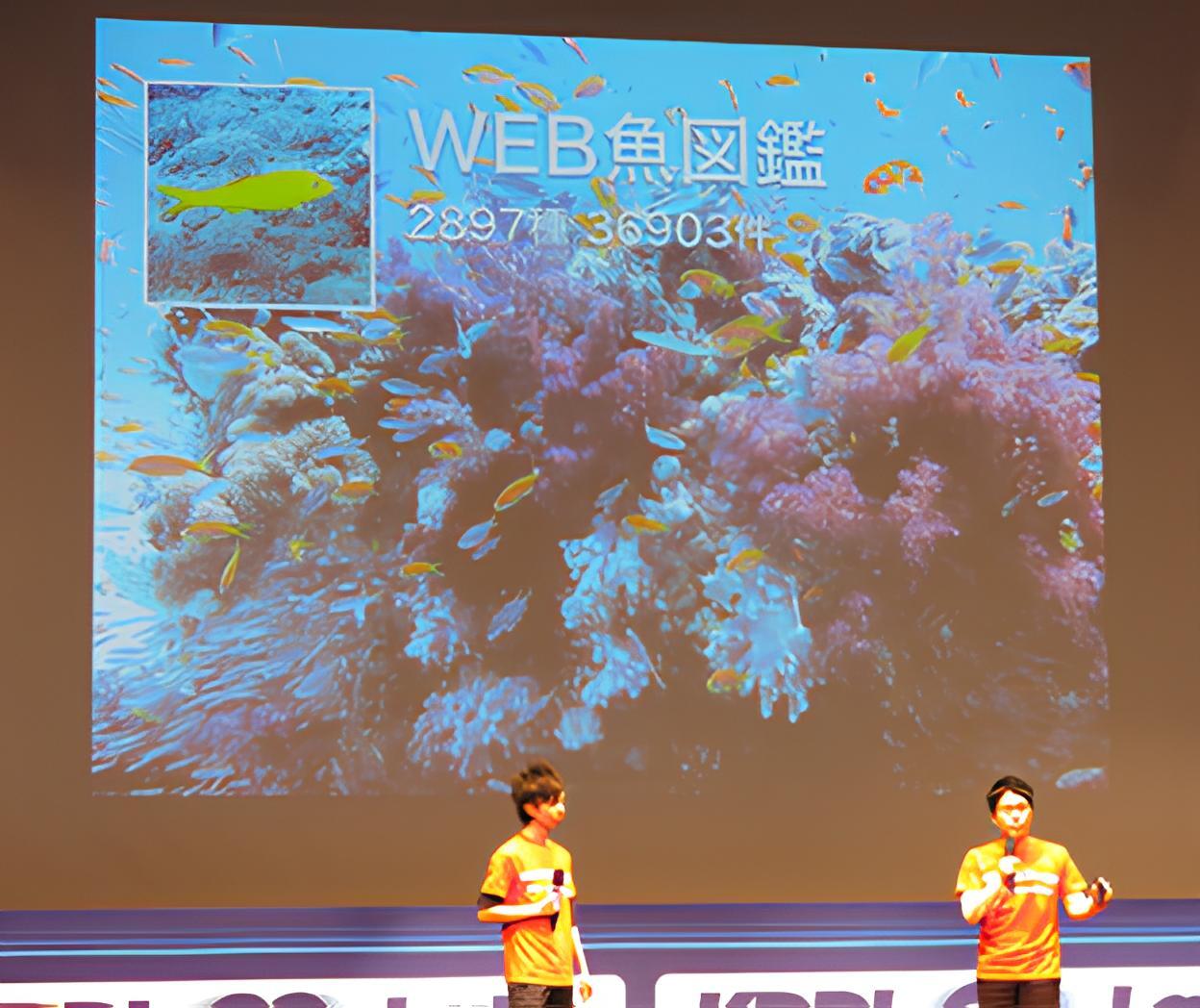 WEB魚図鑑の紹介スライドを前に登壇するスタッフ